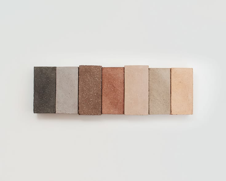 Sept briques de teintes différentes, du brun foncé au rose pâle, alignées côte à côte sur un fond clair.