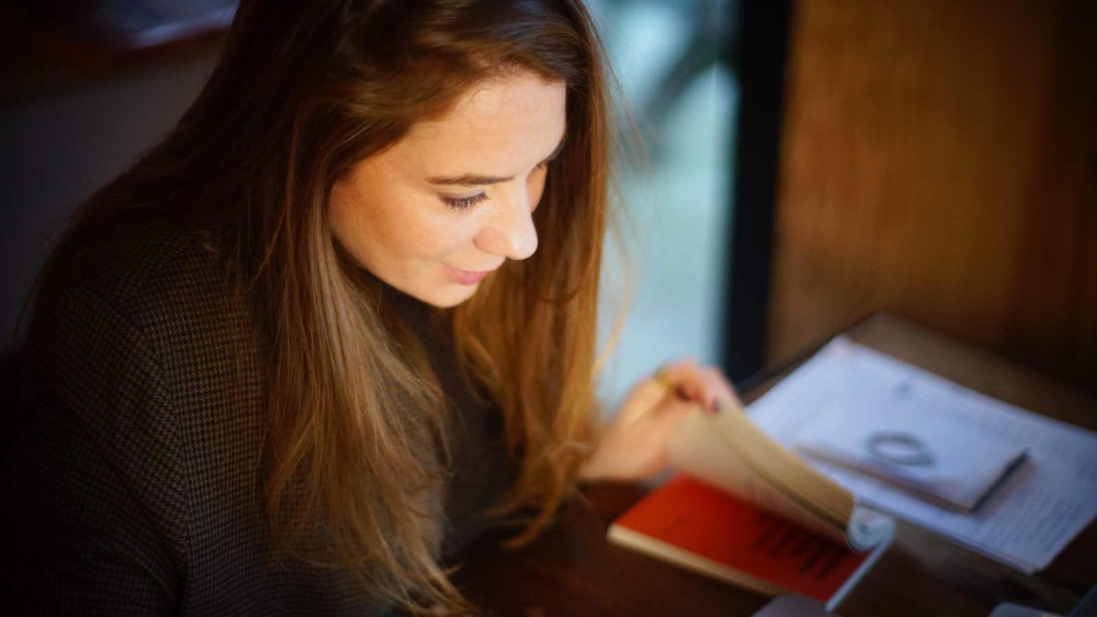 Margot Dandieu de profil, penchée sur un carnet ouvert qu’elle annote, dans une lumière chaude.