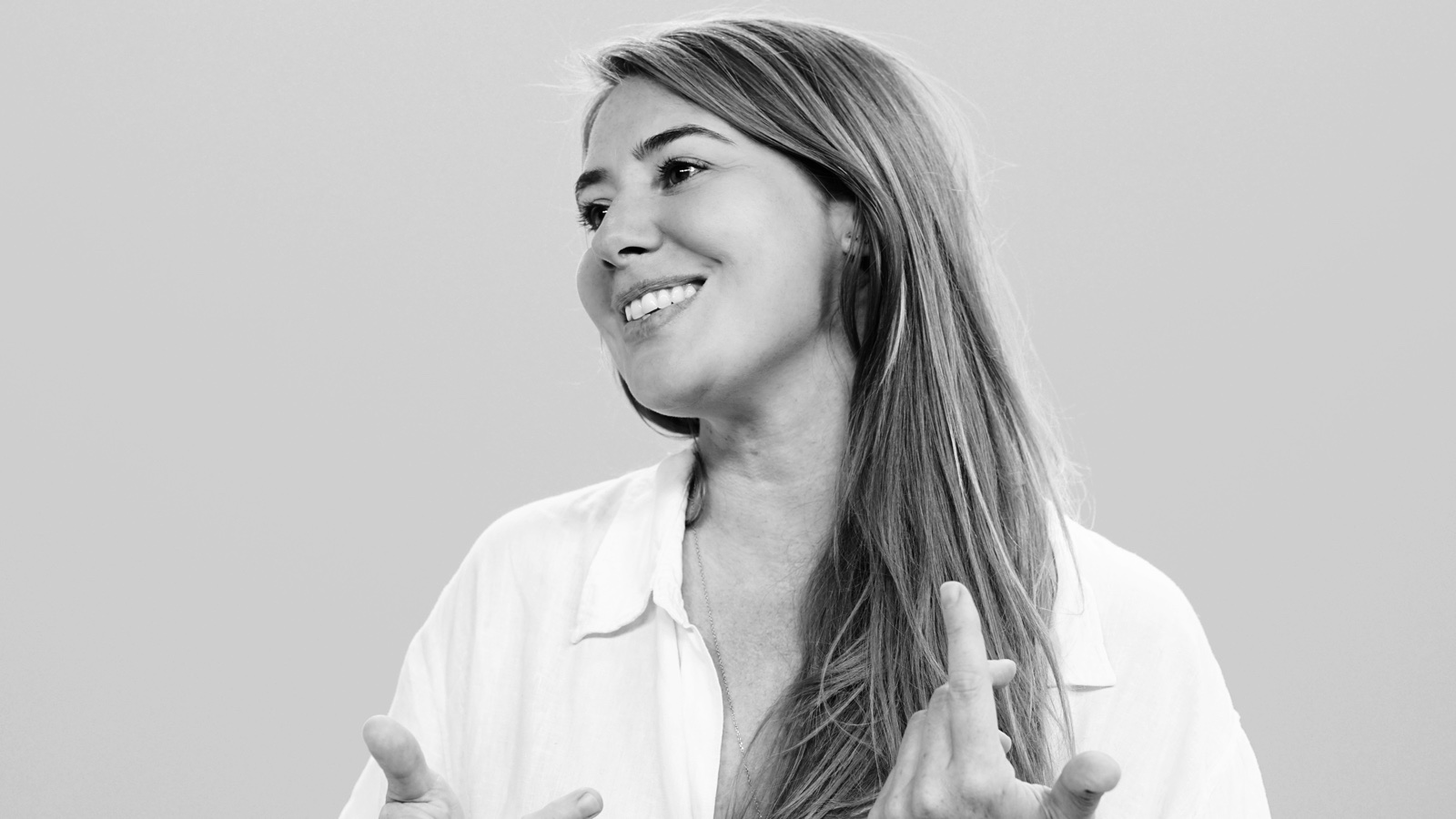 Portrait de Margot Dandieu en noir et blanc, souriante, les mains levées en train de parler.